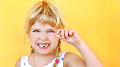 Young girl smiling with a gap in her teeth, holding a lost baby tooth